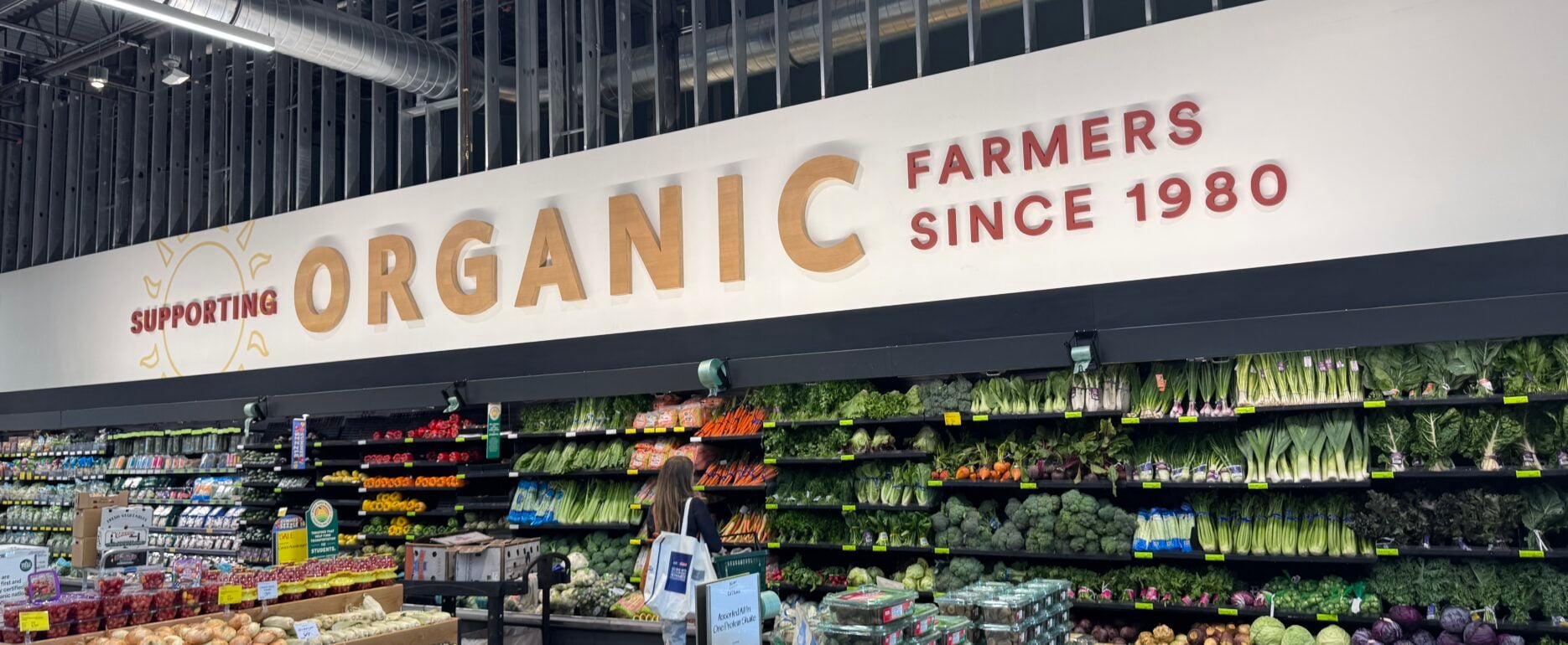 Interior of a grocery store produce section with shelves of fruits and vegetables and an 'ORGANIC' sign in the background