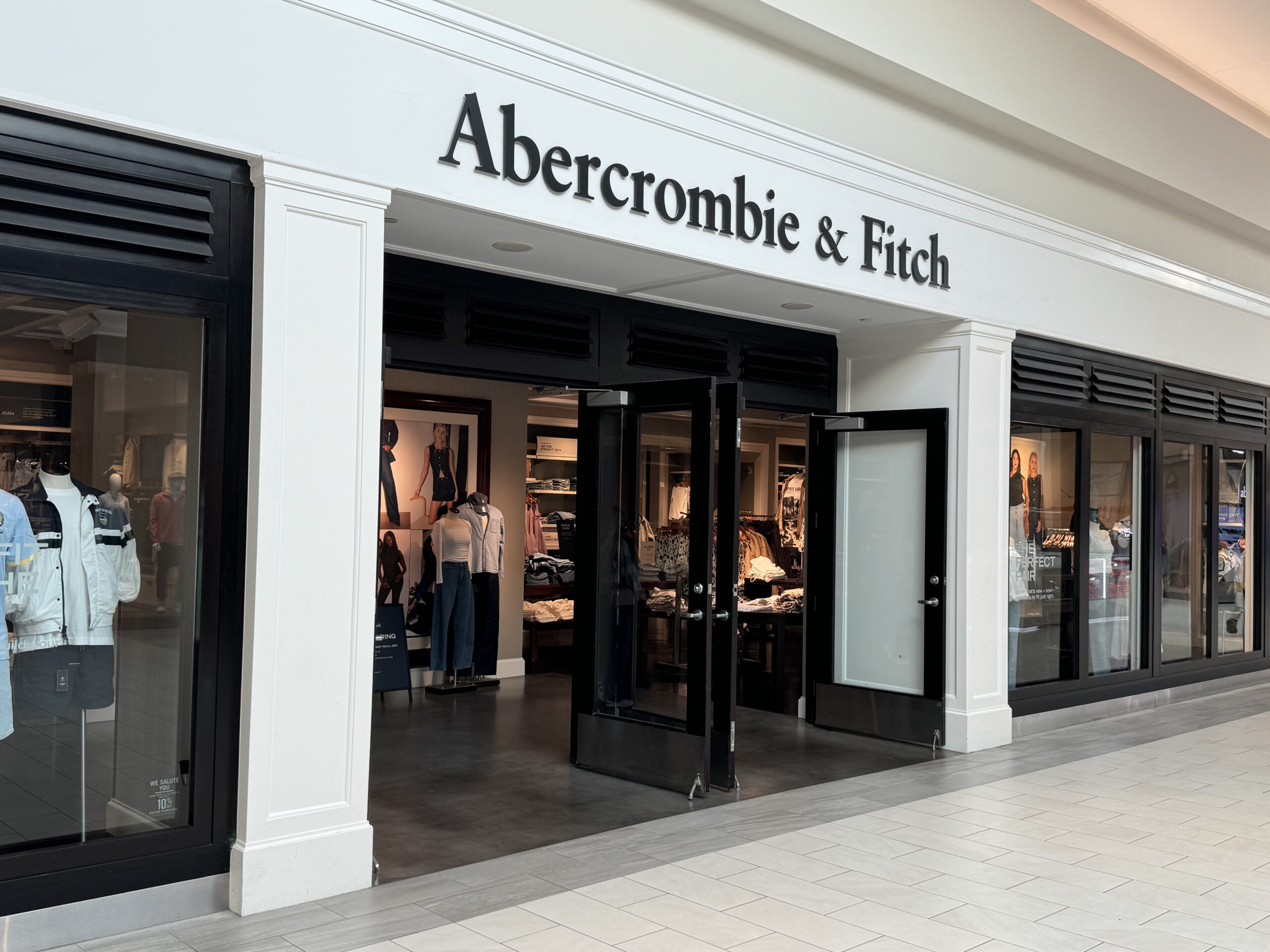Abercrombie & Fitch storefront in a mall, with mannequins and clothing on display behind glass windows and open doors