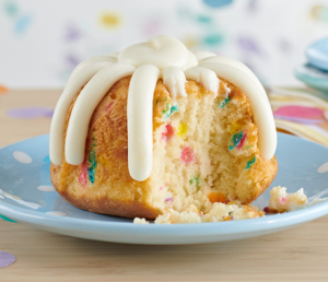 Slice of colorful funfetti cake with white icing drizzle on a blue plate.