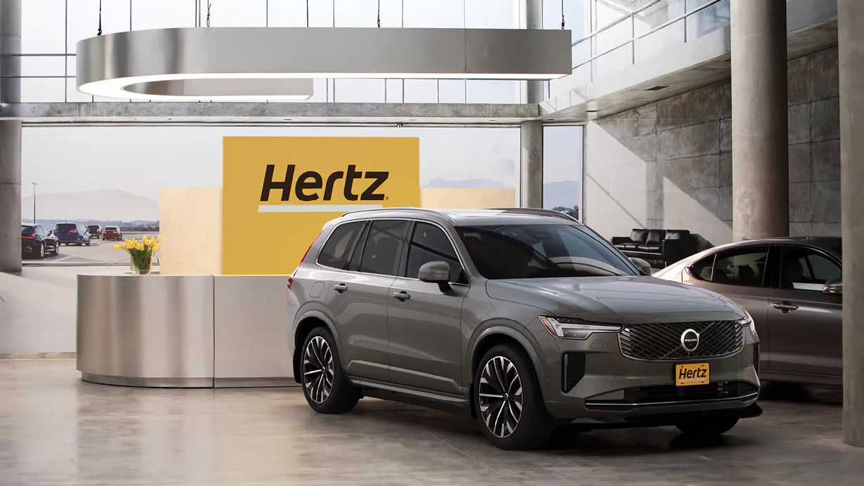 Grey SUV on display inside Hertz showroom with a yellow Hertz sign in the background