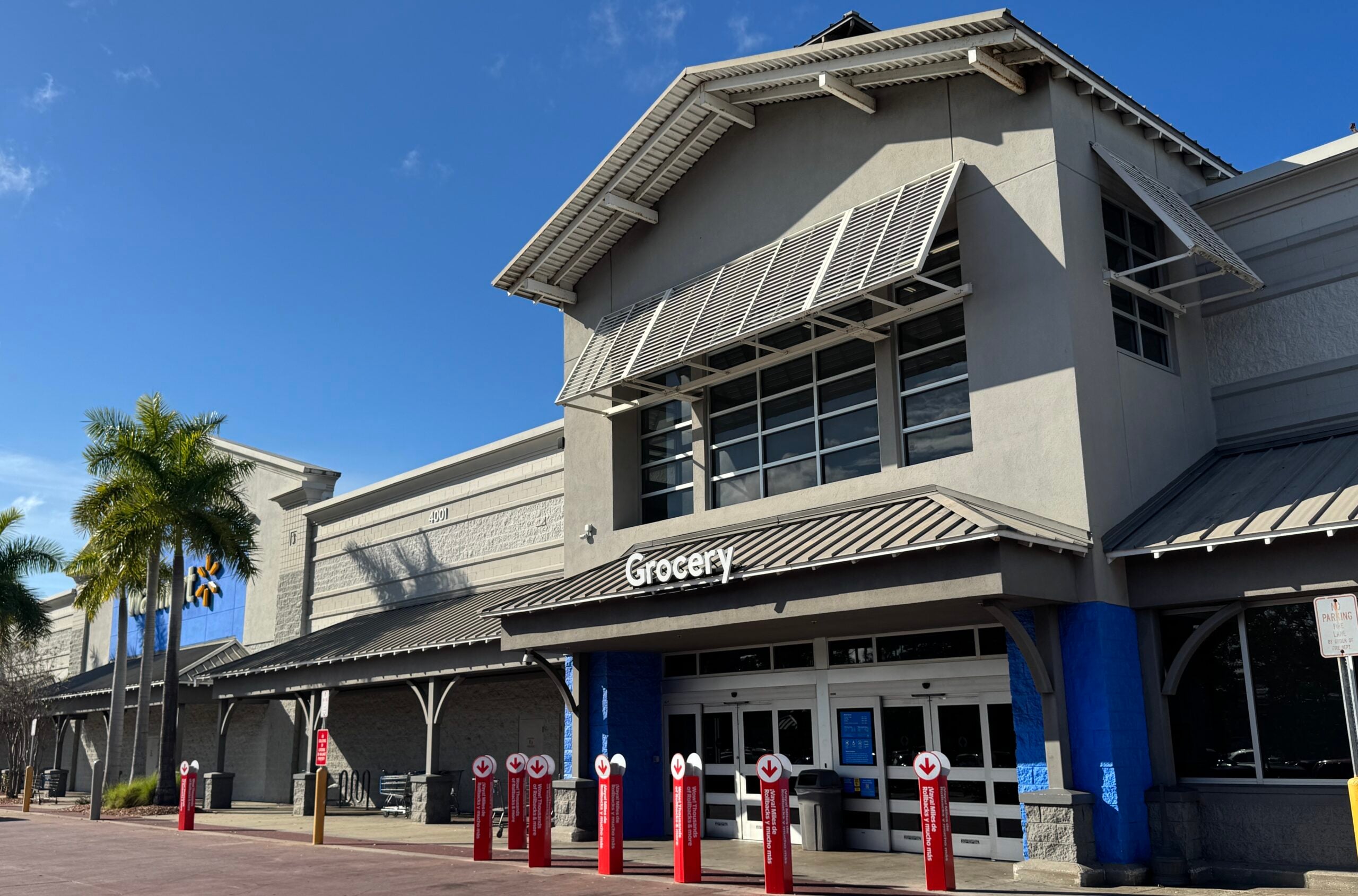 Exterior of a Walmart Grocery store with a row of red safety bollards in front and palm trees nearby on a bright day.